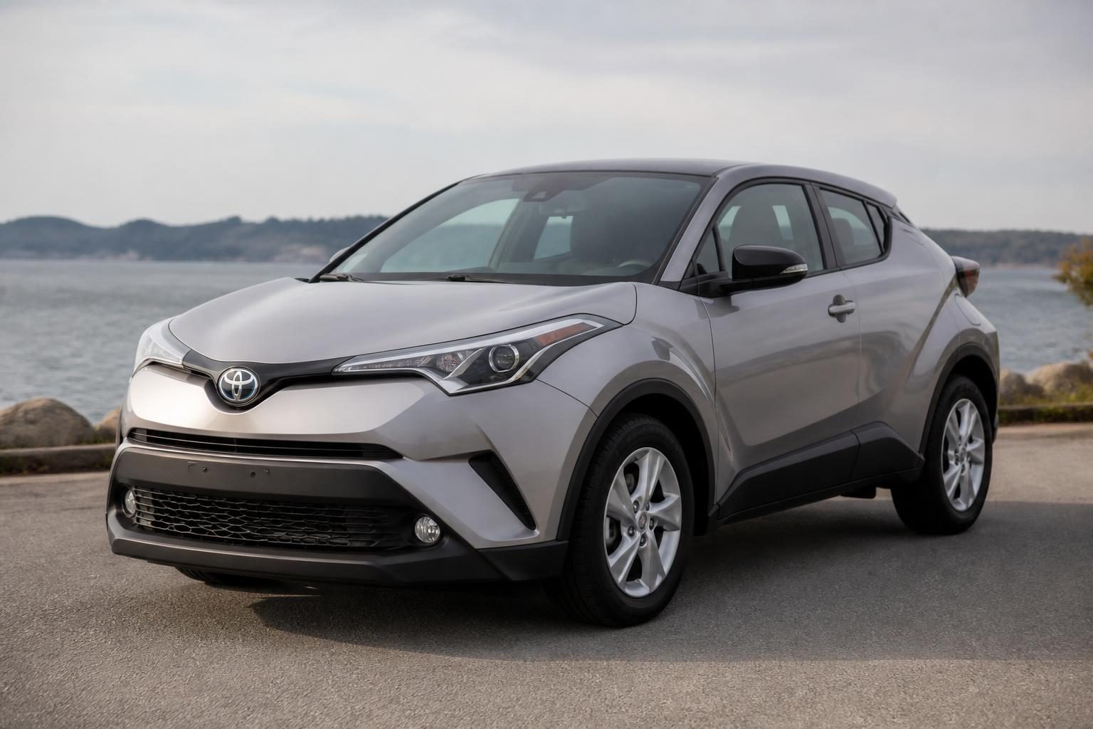 Silver Toyota C-HR crossover parked on a road beside water, viewed from the front left.