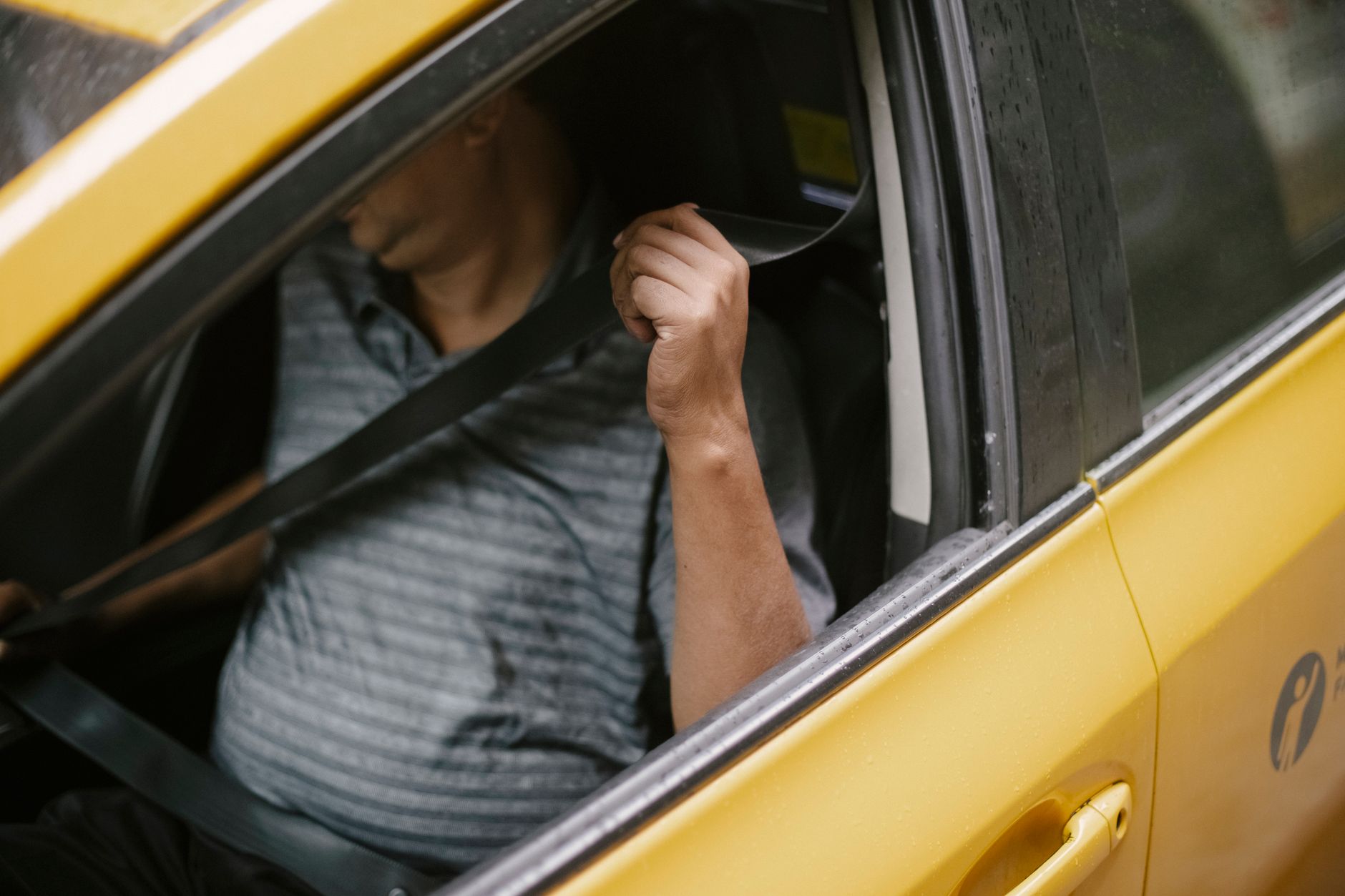 Person in the driver's seat of a yellow car pulling a seatbelt across their chest