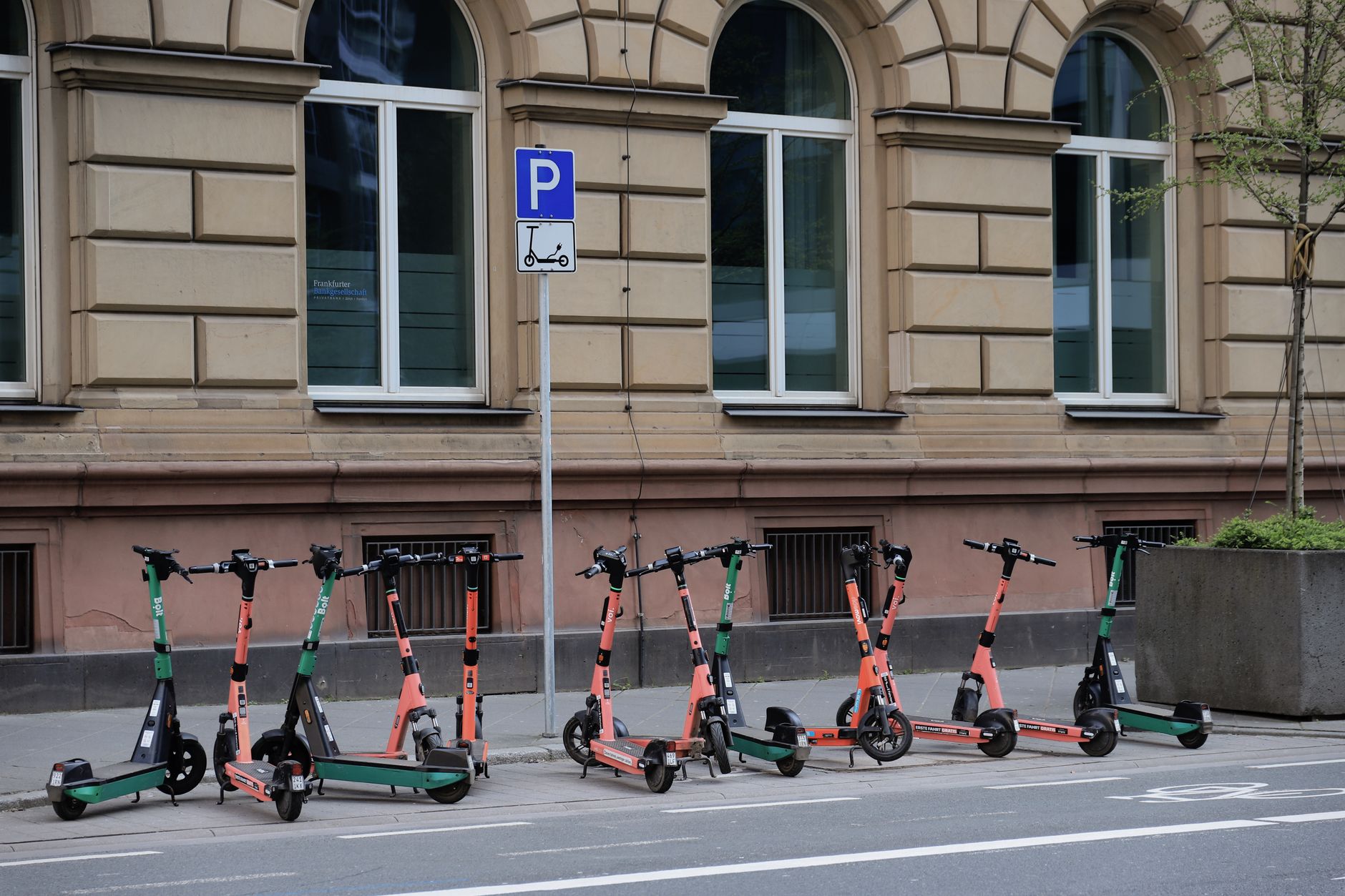 Several parked electric scooters lined up on a footpath beside a street and parking sign
