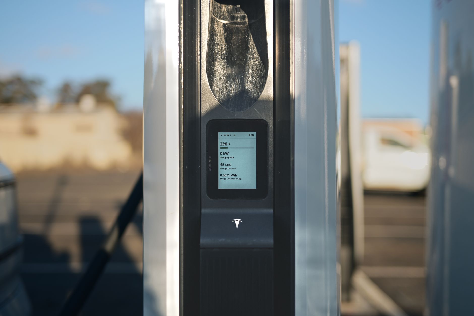 An electric car is plugged into a public fast charger beside a roadside charging bay.