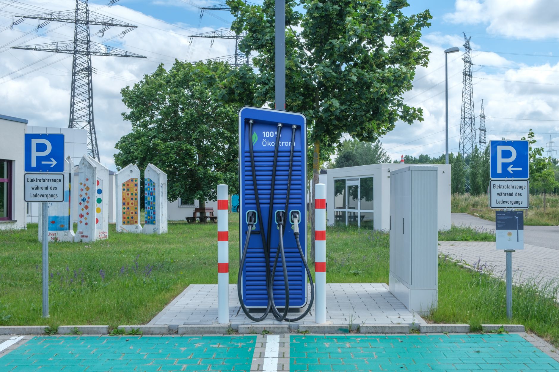 Blue public EV charging station with cables between marked parking spaces beside a road