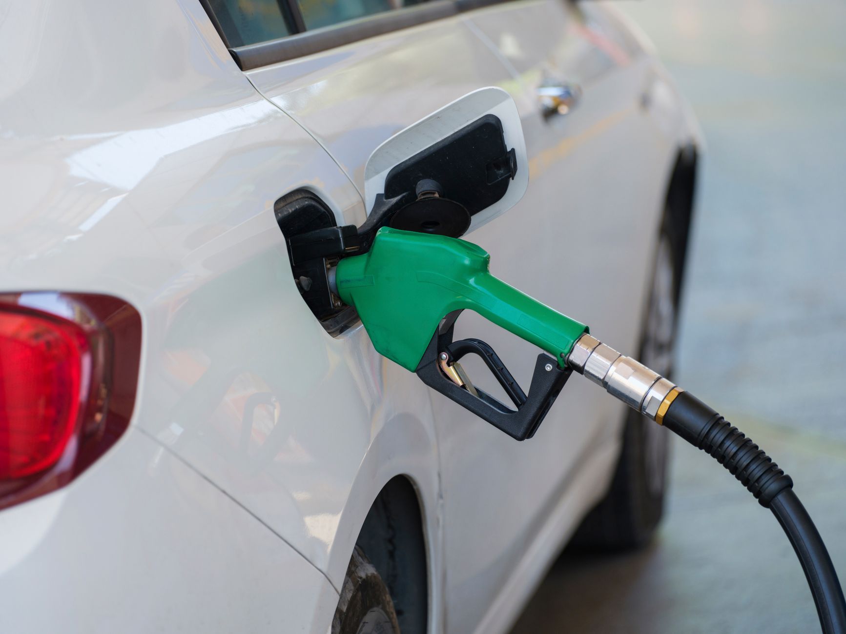 Green petrol nozzle inserted into the open fuel filler of a white car.