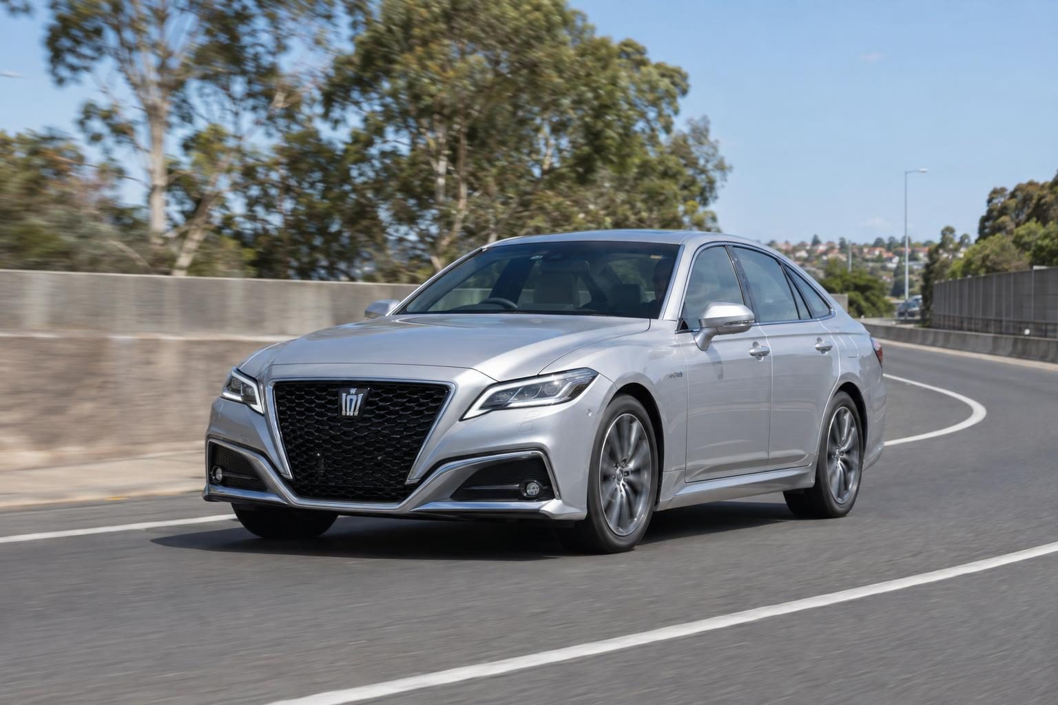 Silver Toyota Crown Hybrid S220 sedan driving on a motorway on-ramp.