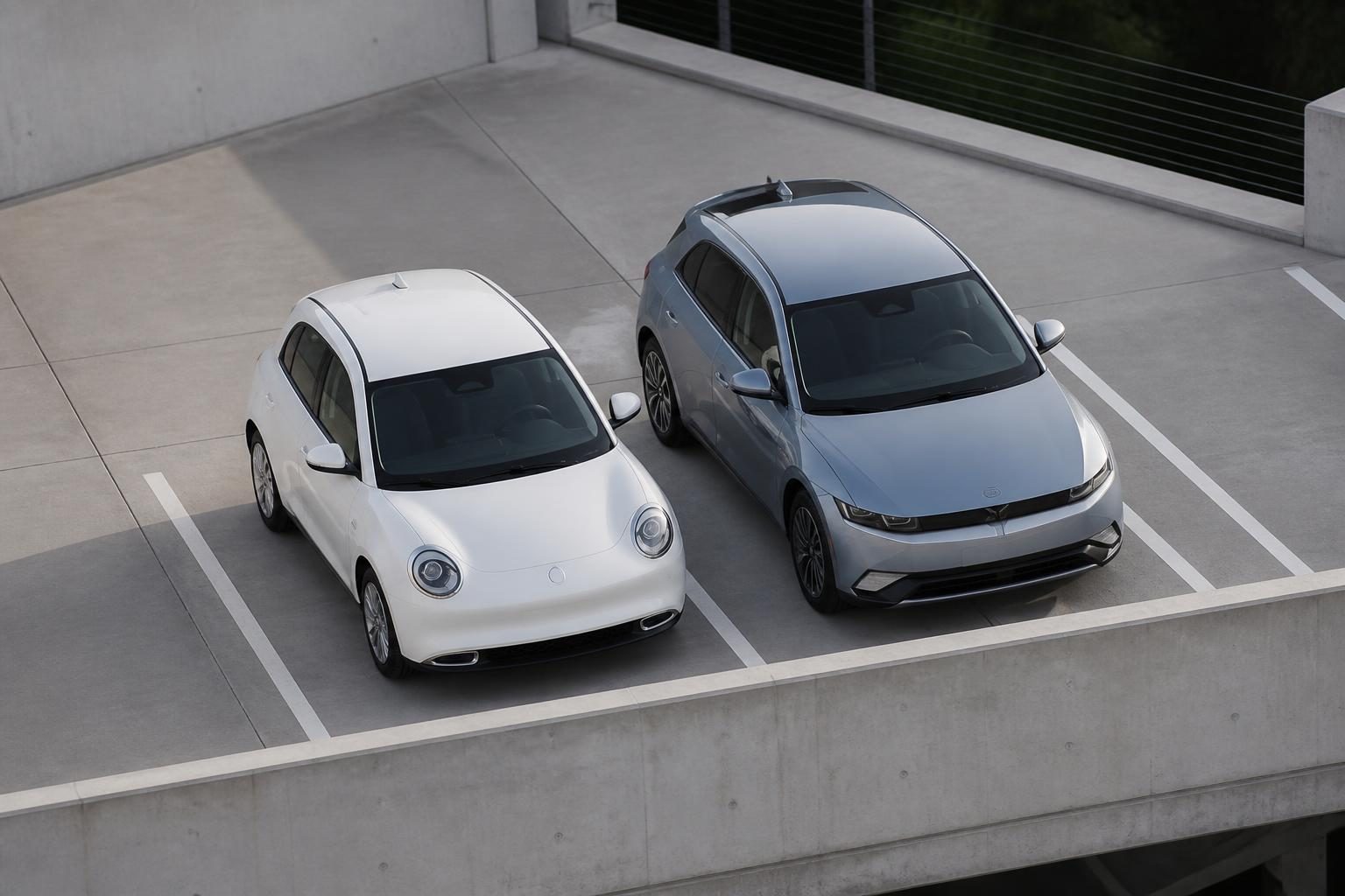 White compact hatchback and silver-blue hatchback parked side by side in a concrete carpark.