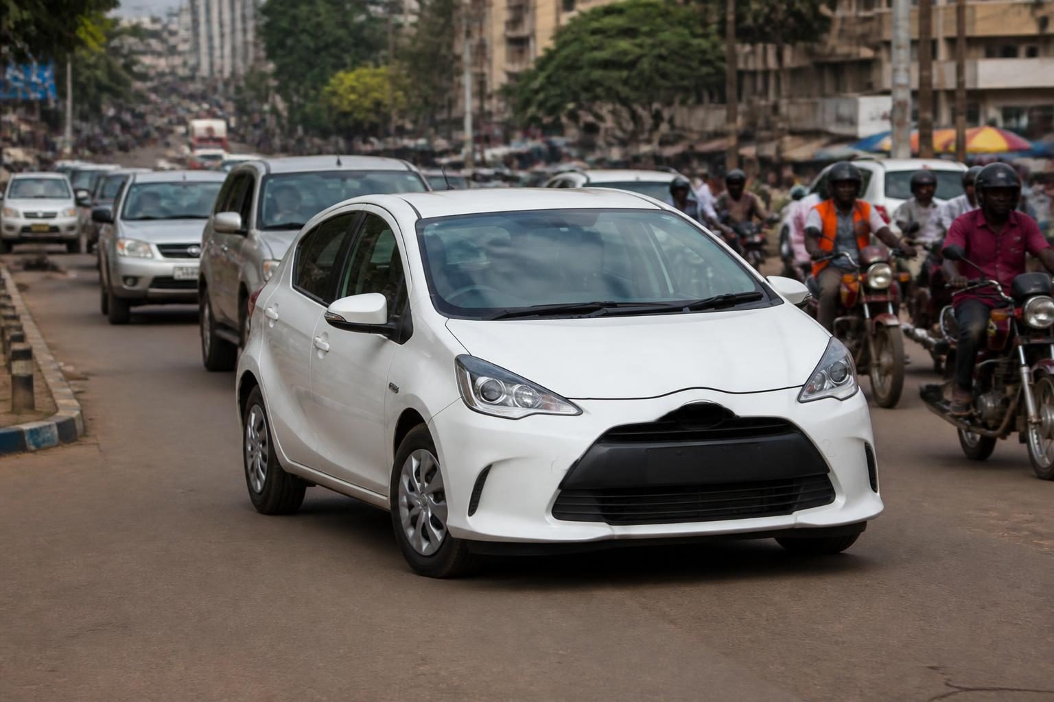 White compact hatchback driving amid motorcycle traffic on a busy city street