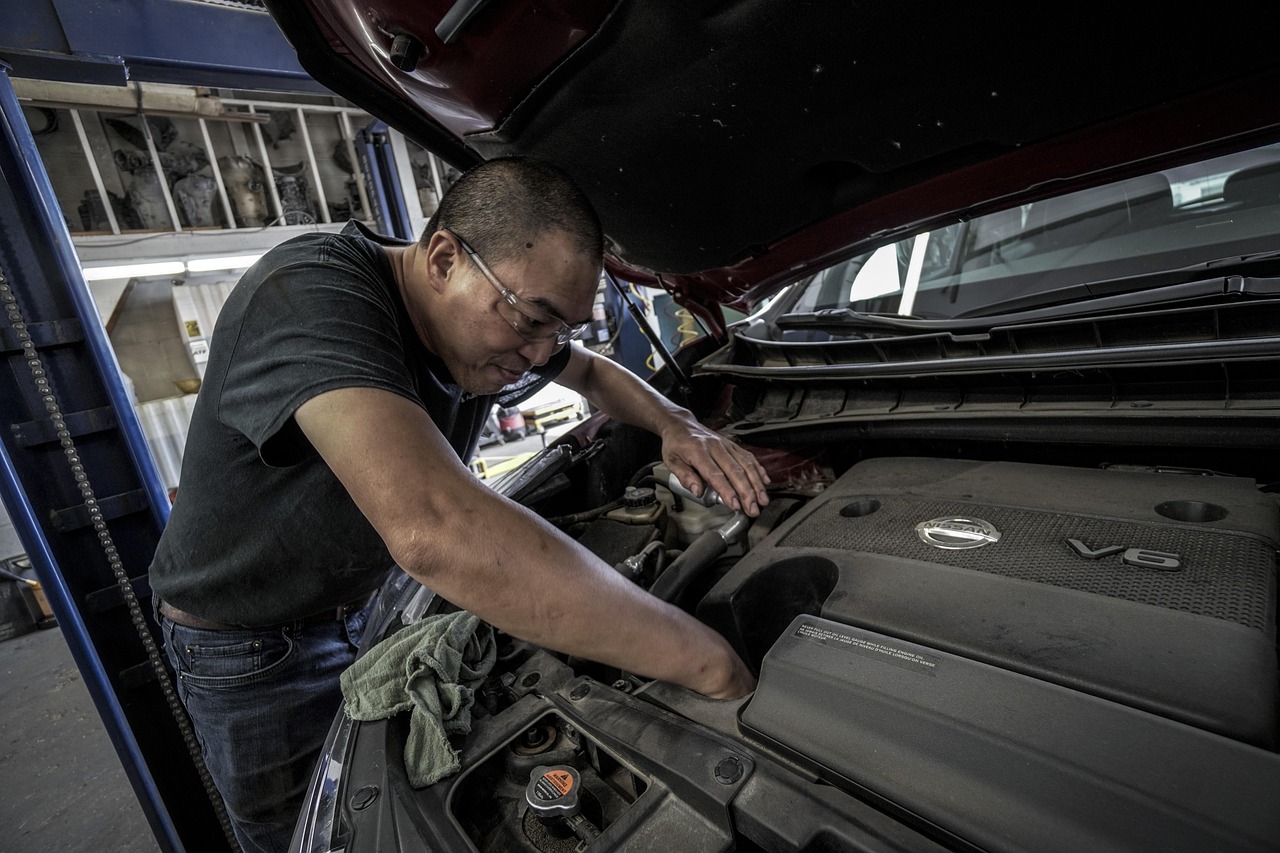 Mechanic leaning over an open car hood while working on the engine in a workshop.