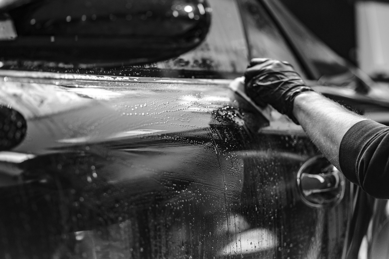 Gloved hand wiping water from a wet black car door and window.