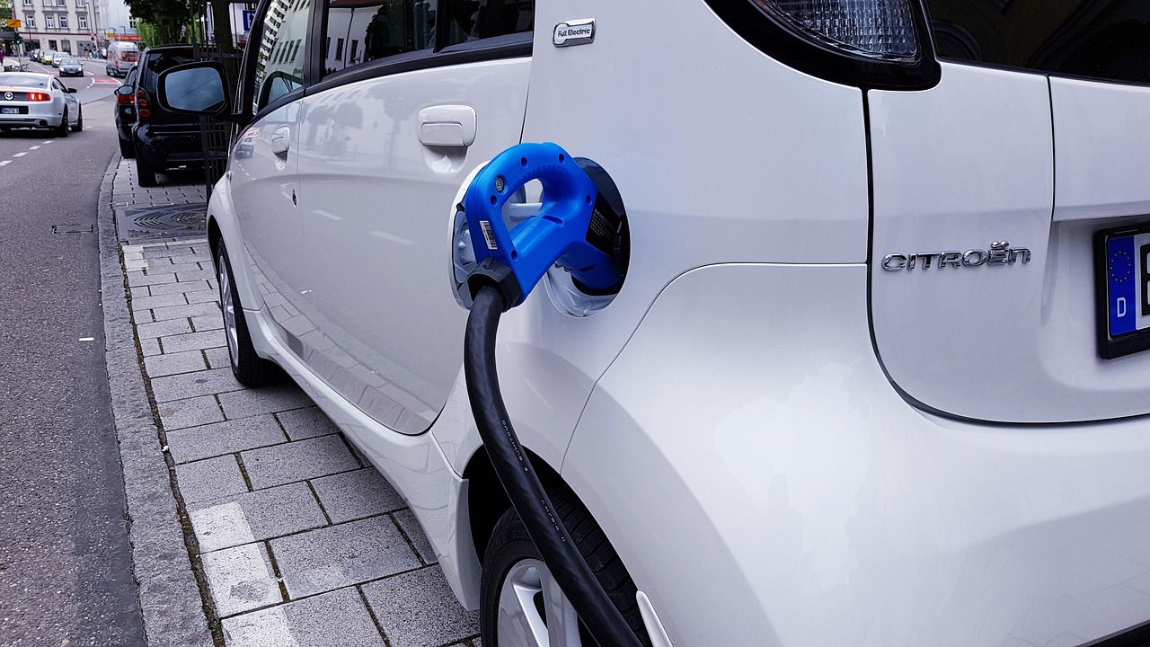 White electric car plugged into a charging cable while parked along a city street