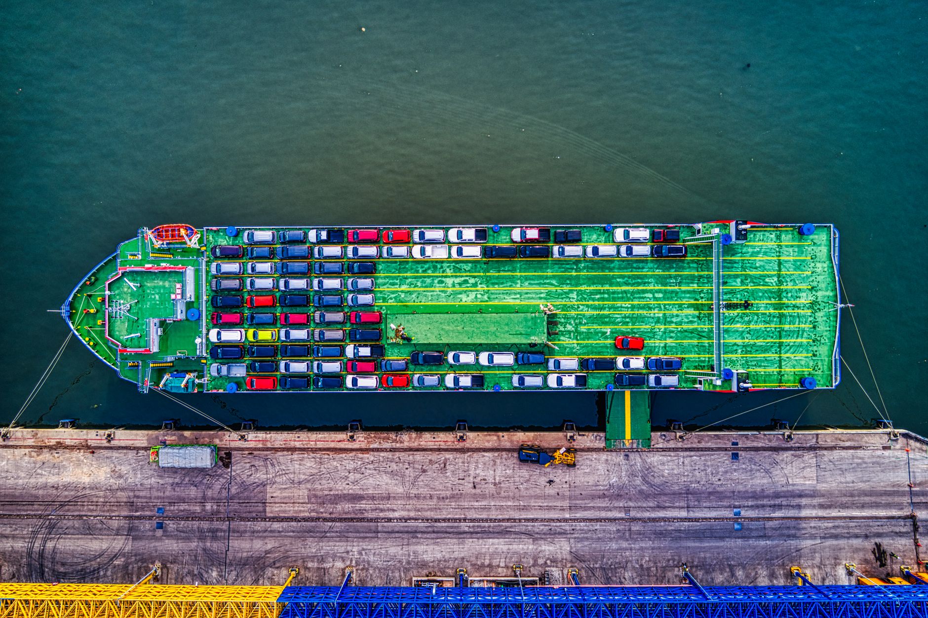 Top-down view of a car carrier ship loaded with vehicles docked at a port quay.