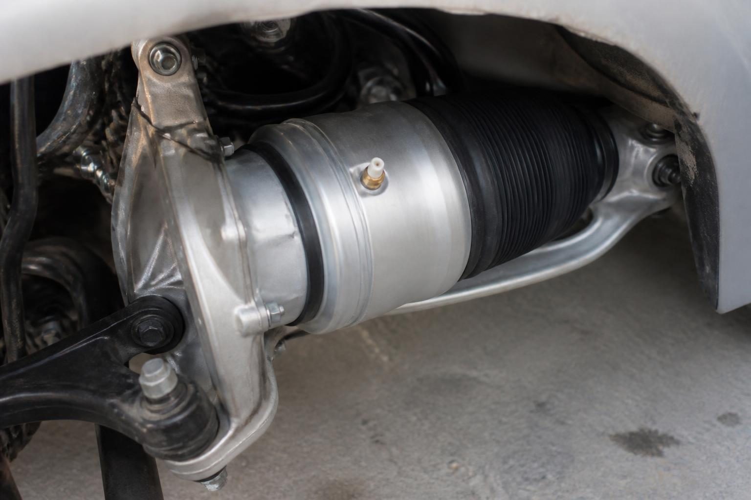 Close-up of a car air suspension strut with black rubber bellows and silver housing in a wheel well