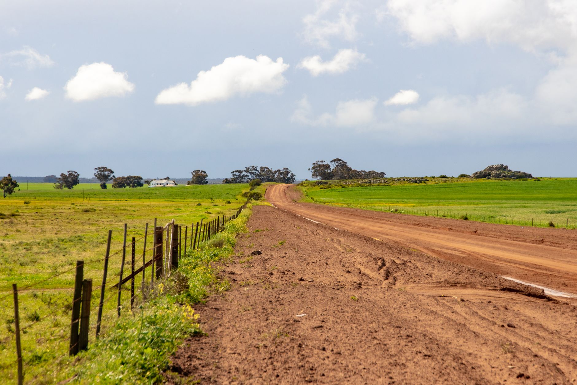 An unpaved rural road winding through green fields beneath a cloudy sky.