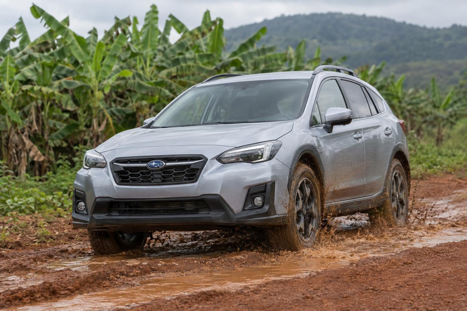 Silver second-generation Subaru XV driving through muddy water on a rutted dirt track.