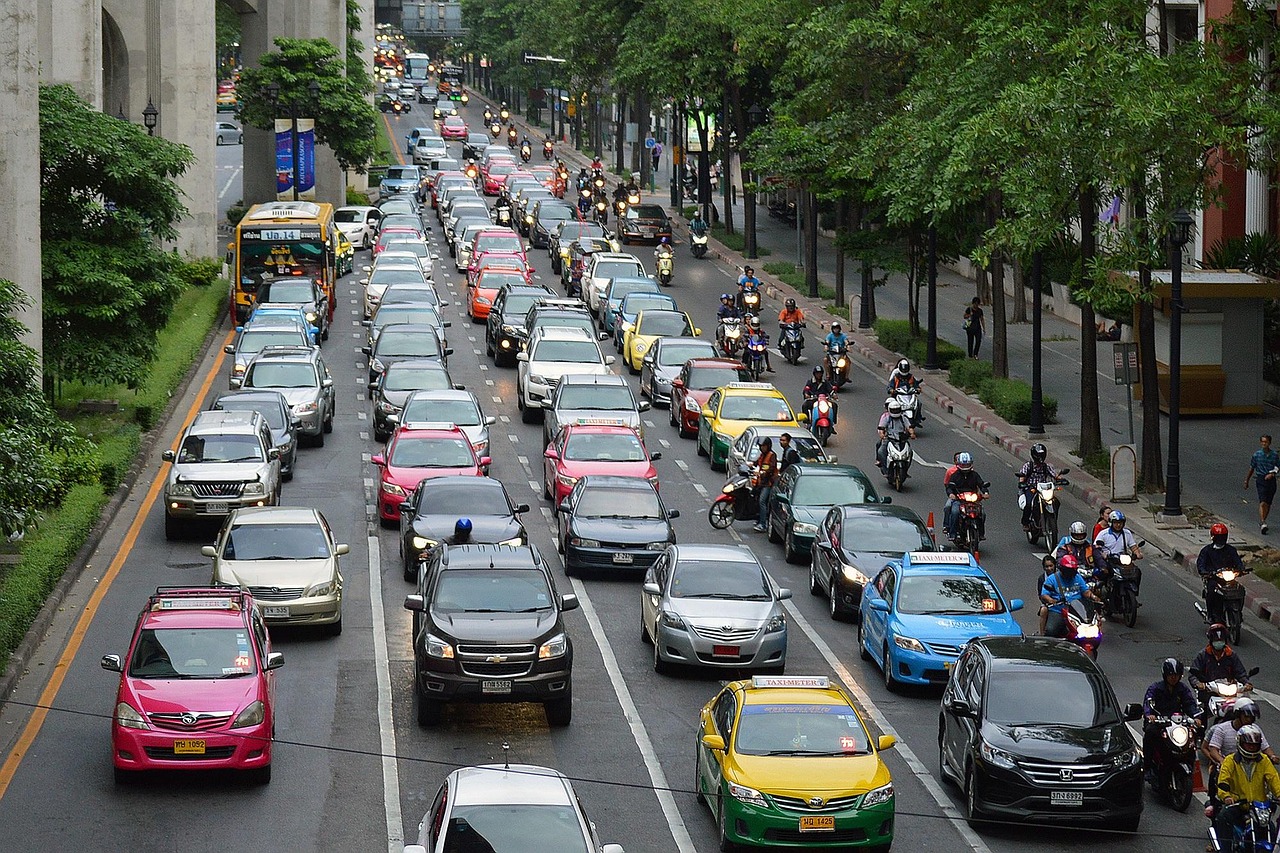 Multi-lane city street packed with cars, taxis, a bus, and motorcycles between tree-lined sidewalks