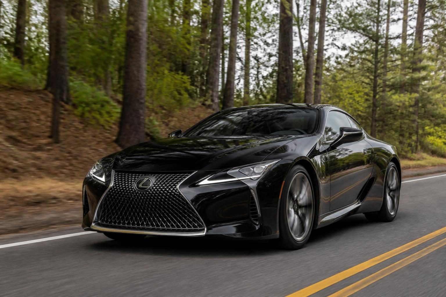 Black Lexus LC coupe driving on a two-lane tree-lined road.