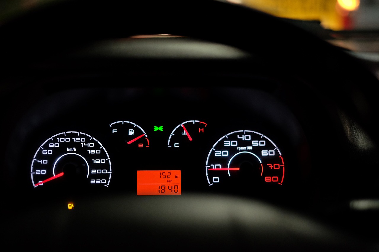 Illuminated car instrument cluster with analog gauges and a digital display reading low kilometres