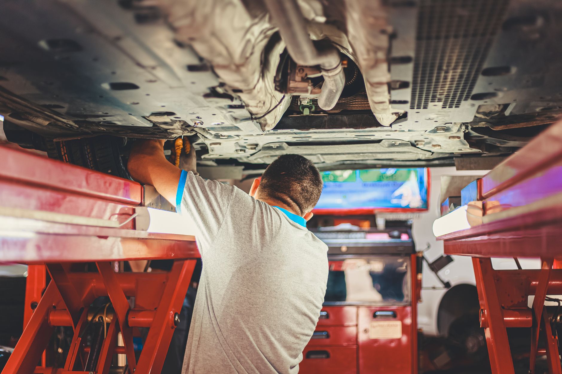 Mechanic examining the underside of a raised car on a red workshop hoist