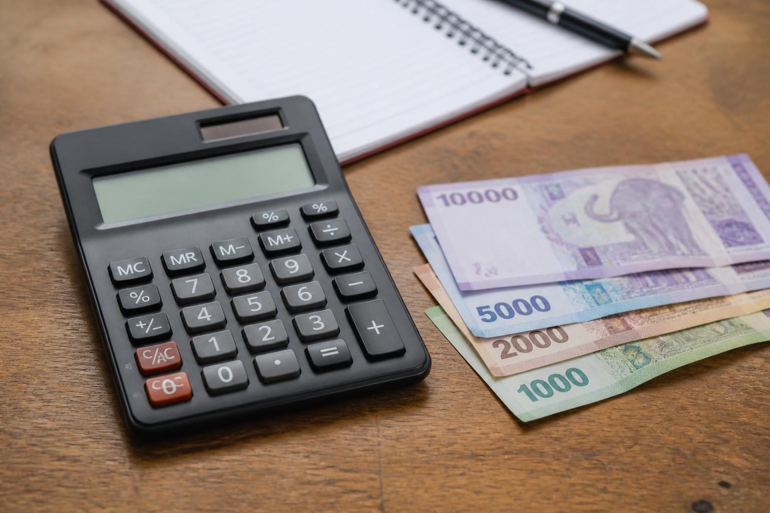 Calculator beside Tanzanian shilling banknotes and an open notebook on a wooden desk.