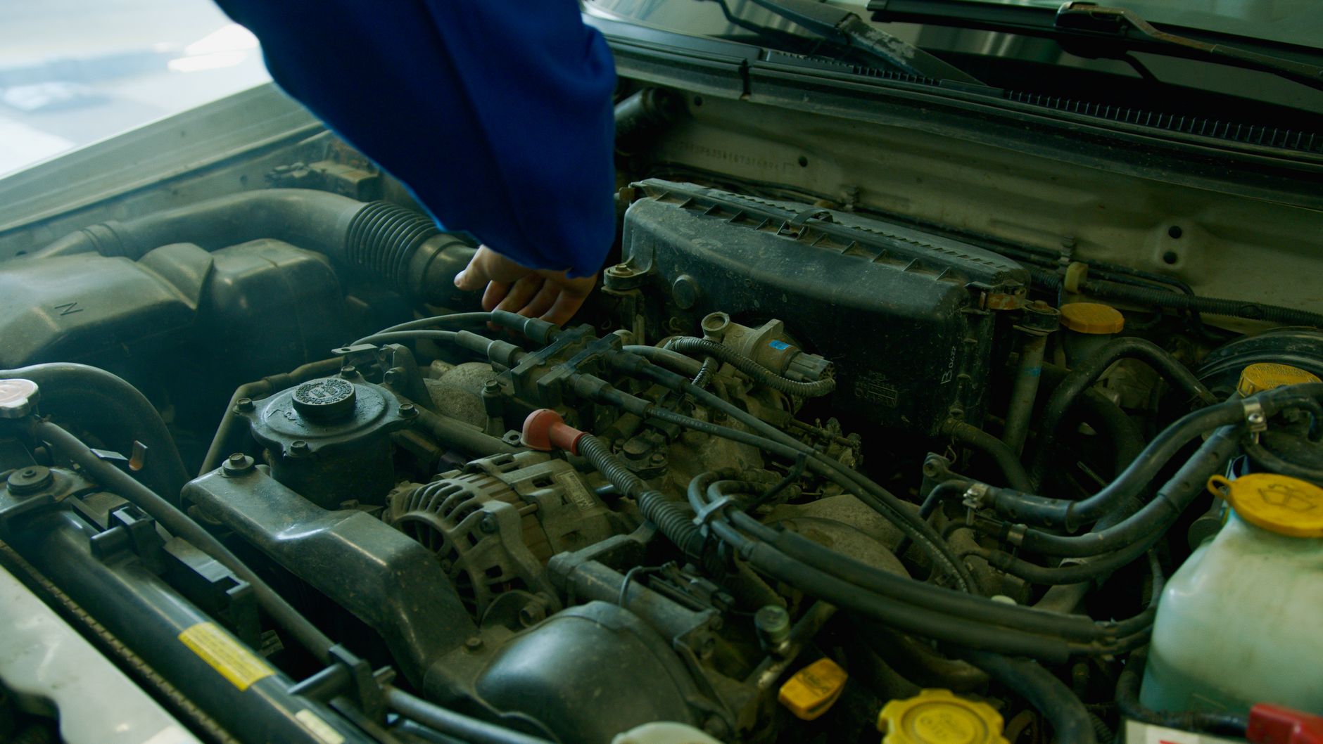 Person in blue sleeve inspecting components inside an open car engine bay