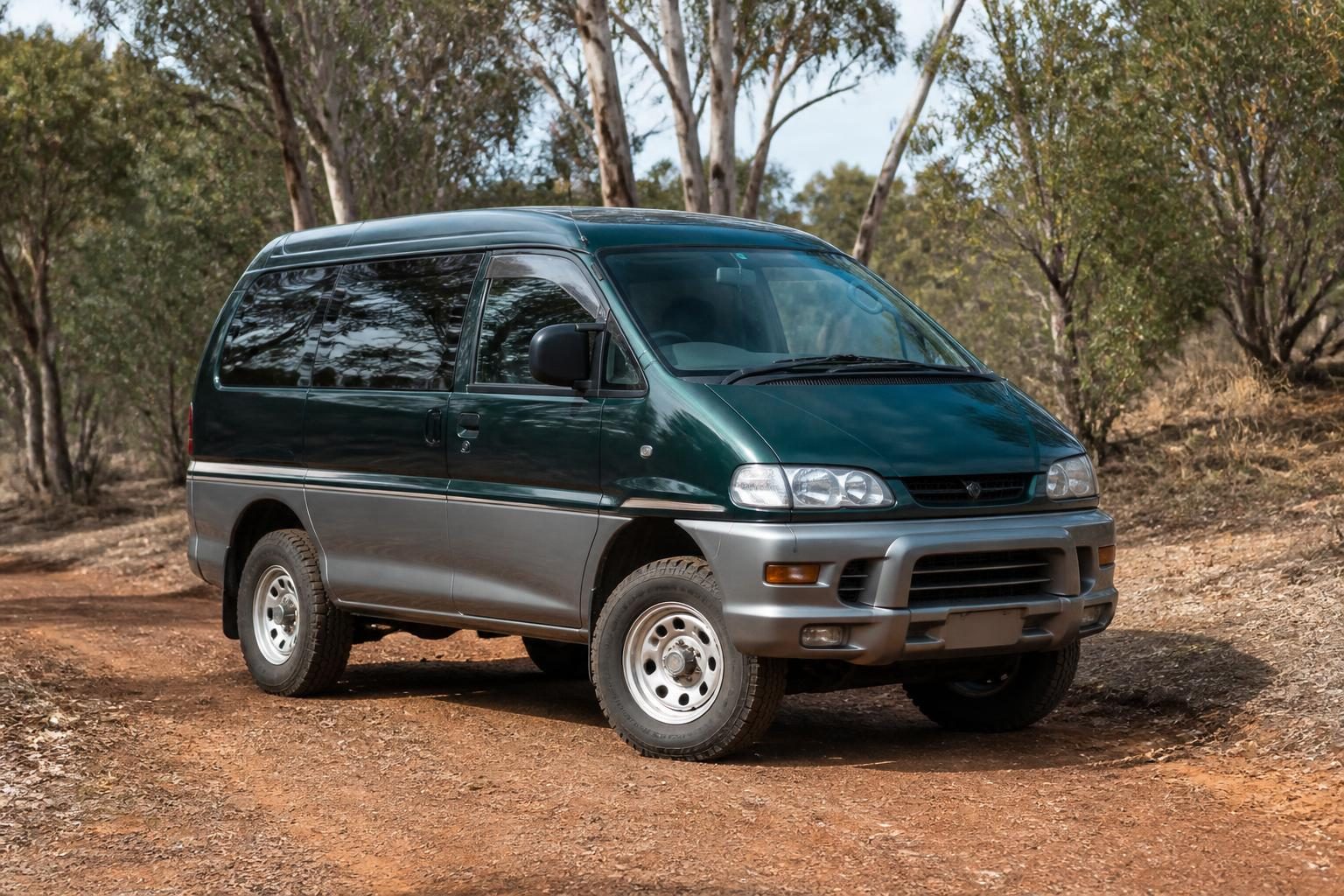 Deep green and grey Mitsubishi Delica van parked on a red-dirt track among eucalyptus trees.