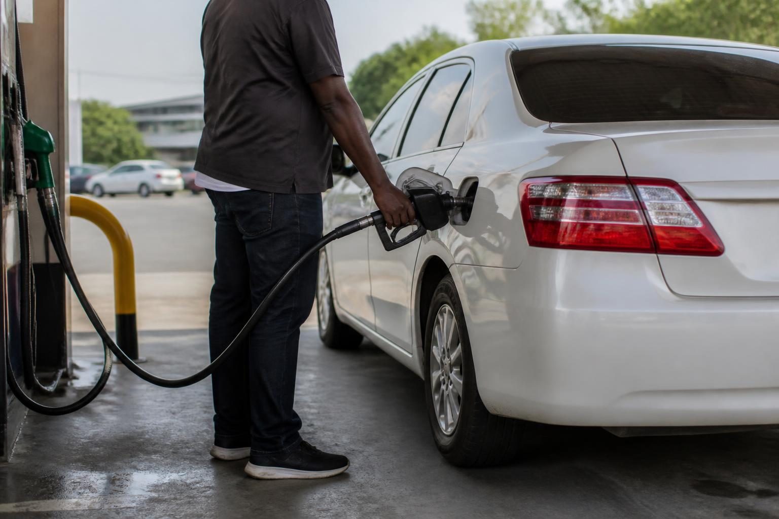 Person refuelling a white sedan at a petrol station, seen from the side and rear