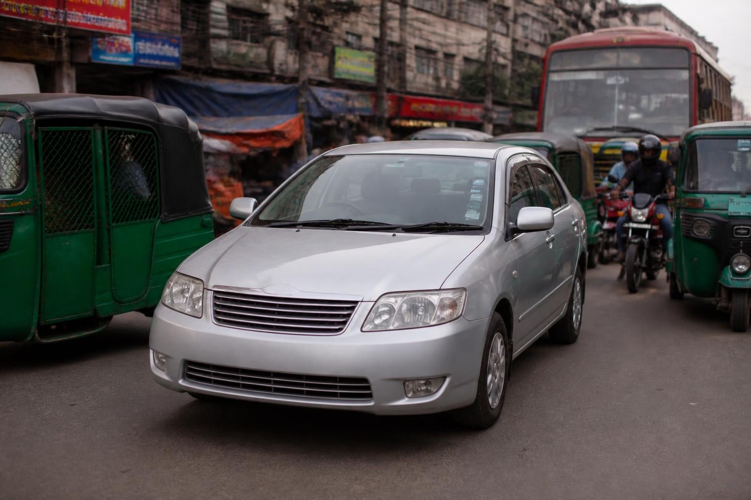 Silver sedan amid green auto-rickshaws, motorcycles and a red bus on a crowded city street.