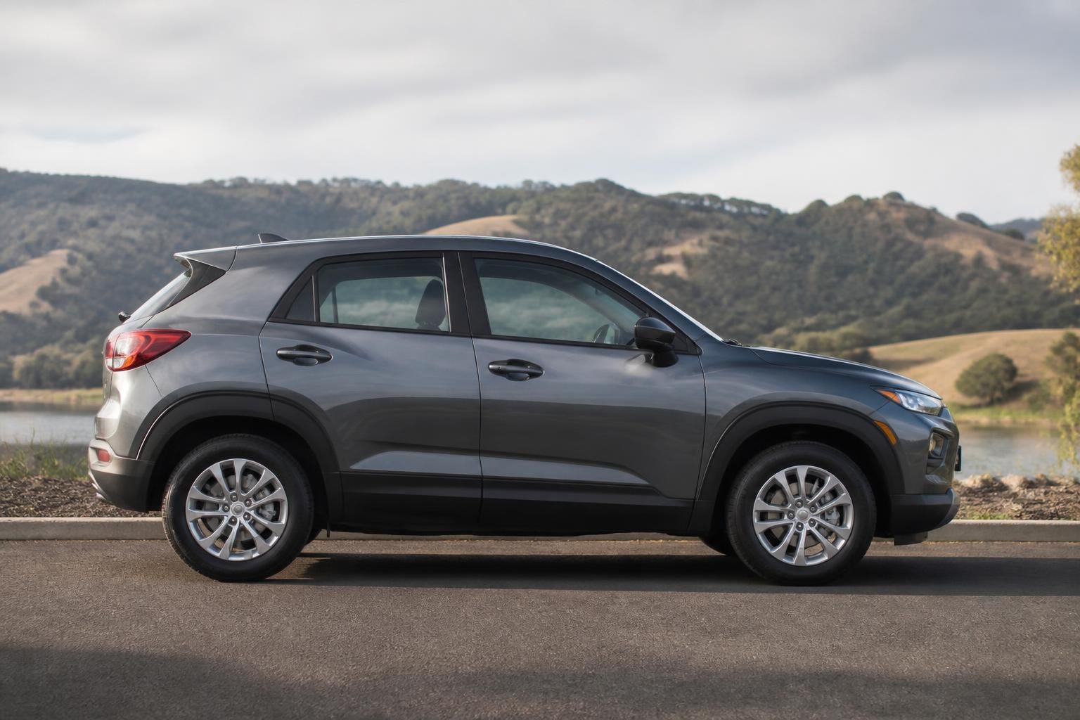 Gray compact crossover SUV shown in side profile on a road beside hills and water.