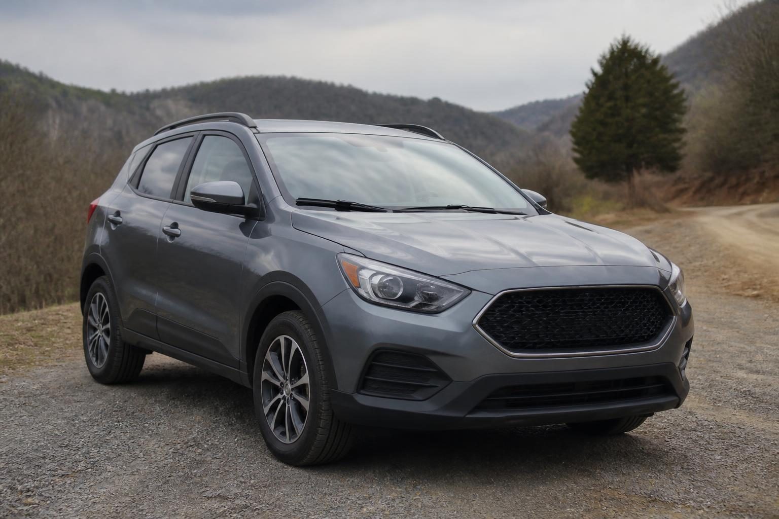 Gray compact crossover SUV parked on a gravel road with wooded mountains behind it.