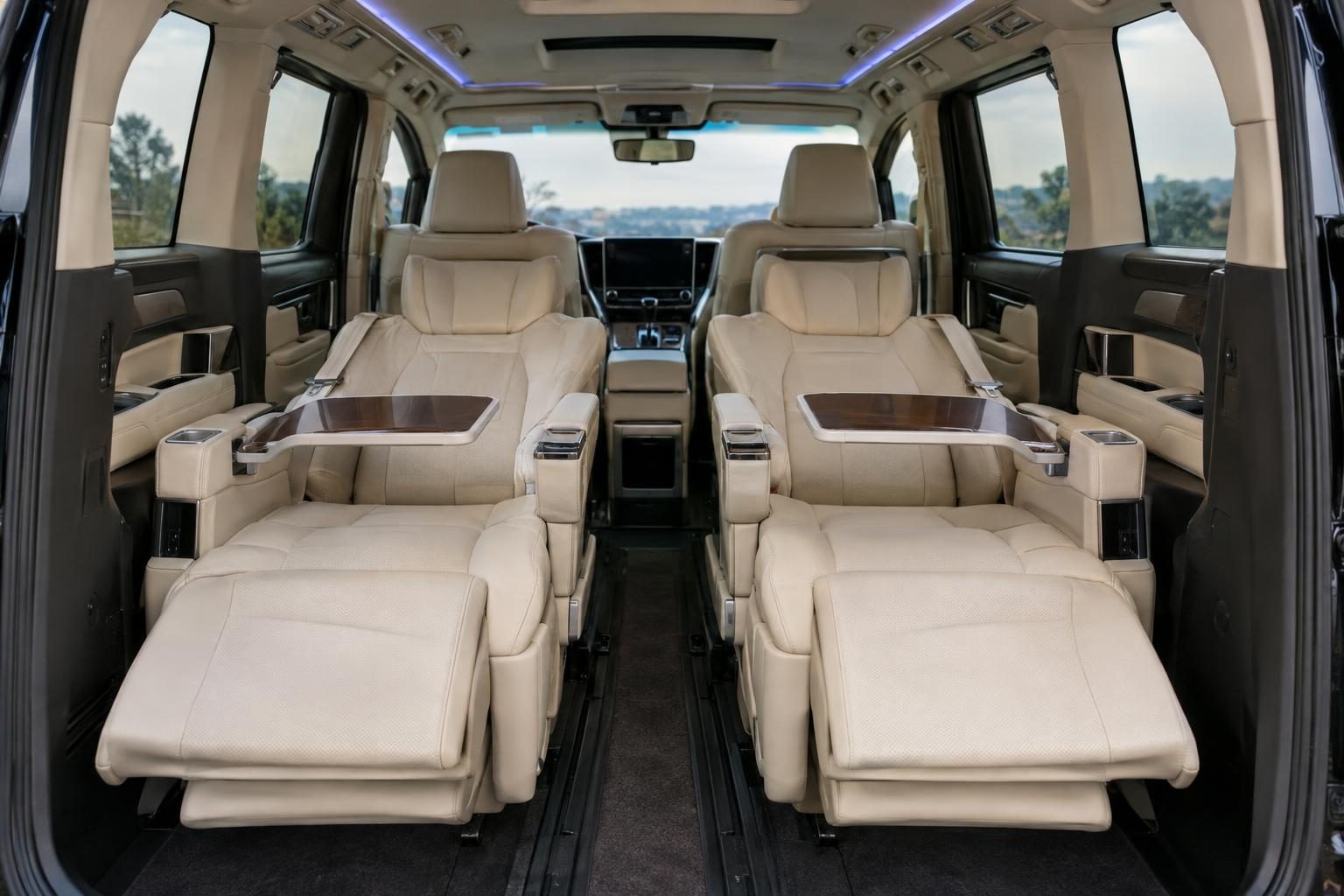 Cream leather second-row captain seats with extended ottomans and tray tables in a Toyota Alphard.