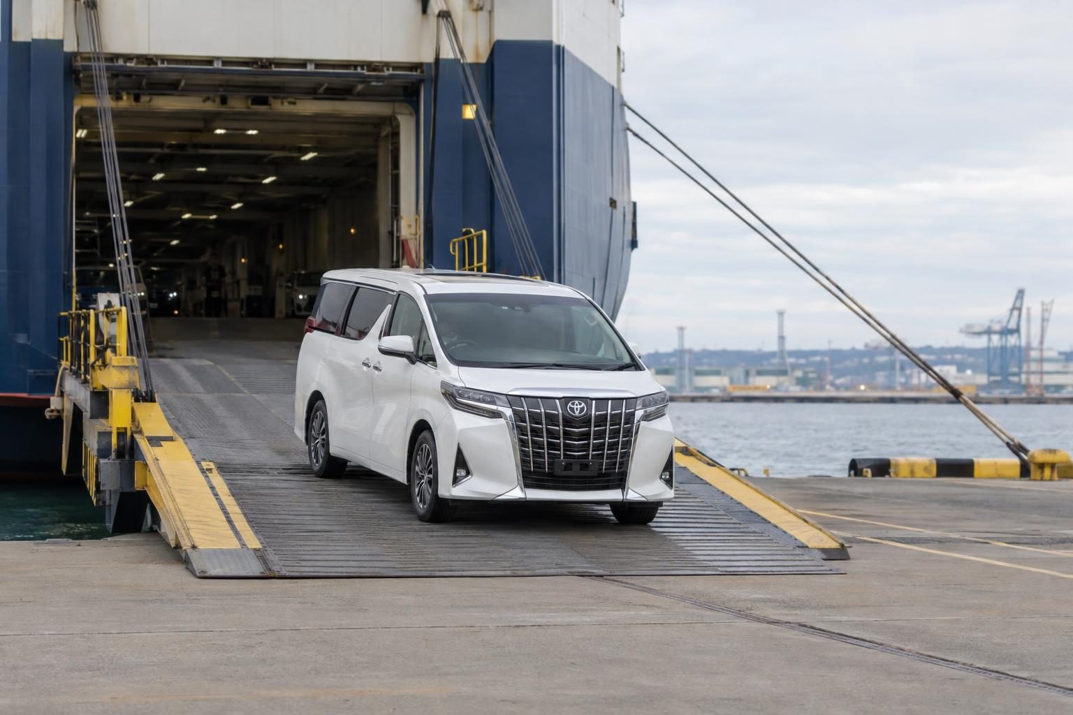 White Toyota Alphard AYH30W driving down a vehicle carrier ramp at a port.
