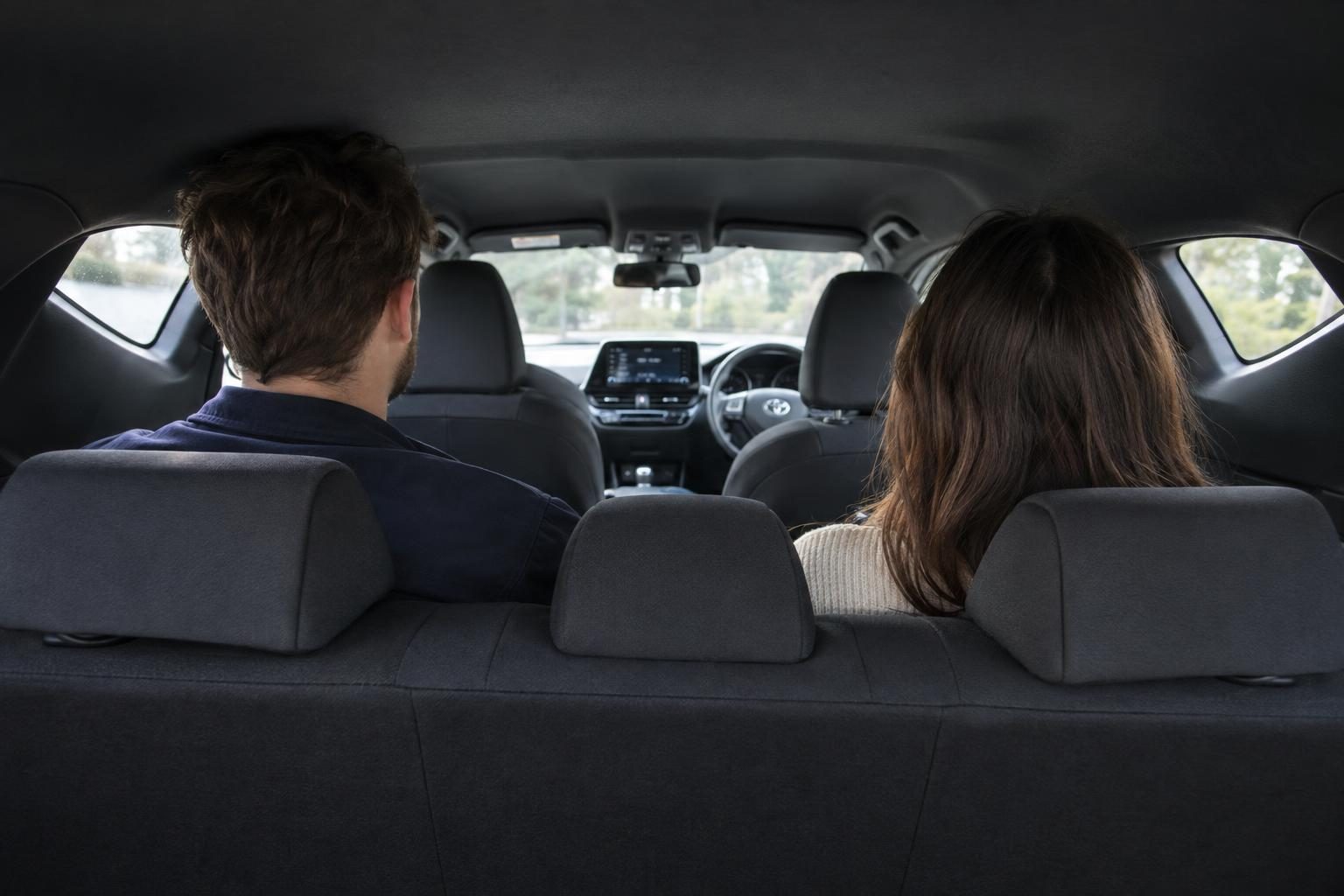 Two adults sit on the rear bench of a Toyota C-HR, viewed forward from the boot.