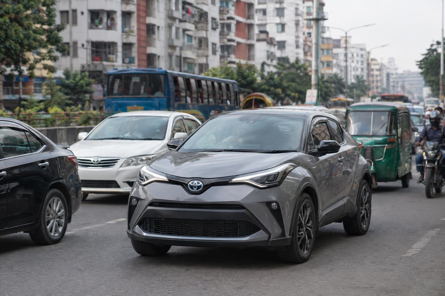 Grey first-generation Toyota C-HR in dense Dhaka traffic with buses and auto-rickshaws.