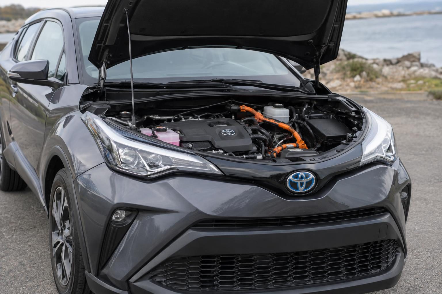 Toyota C-HR hybrid with its bonnet open, showing the engine bay and orange high-voltage cables.