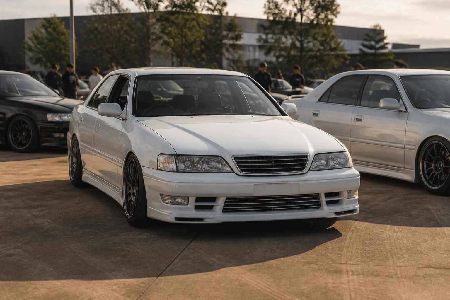 Three modified white and silver Japanese sedans parked side by side at an outdoor car meet.