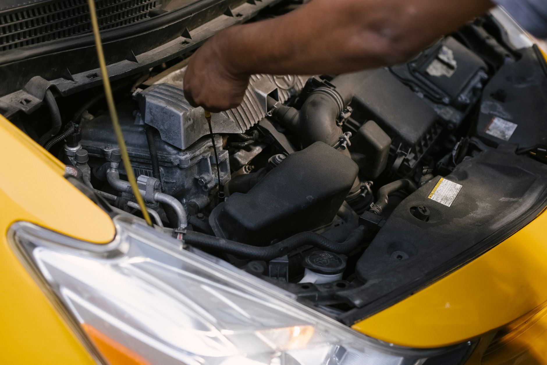 Person's arm reaching into the open engine bay of a yellow car.