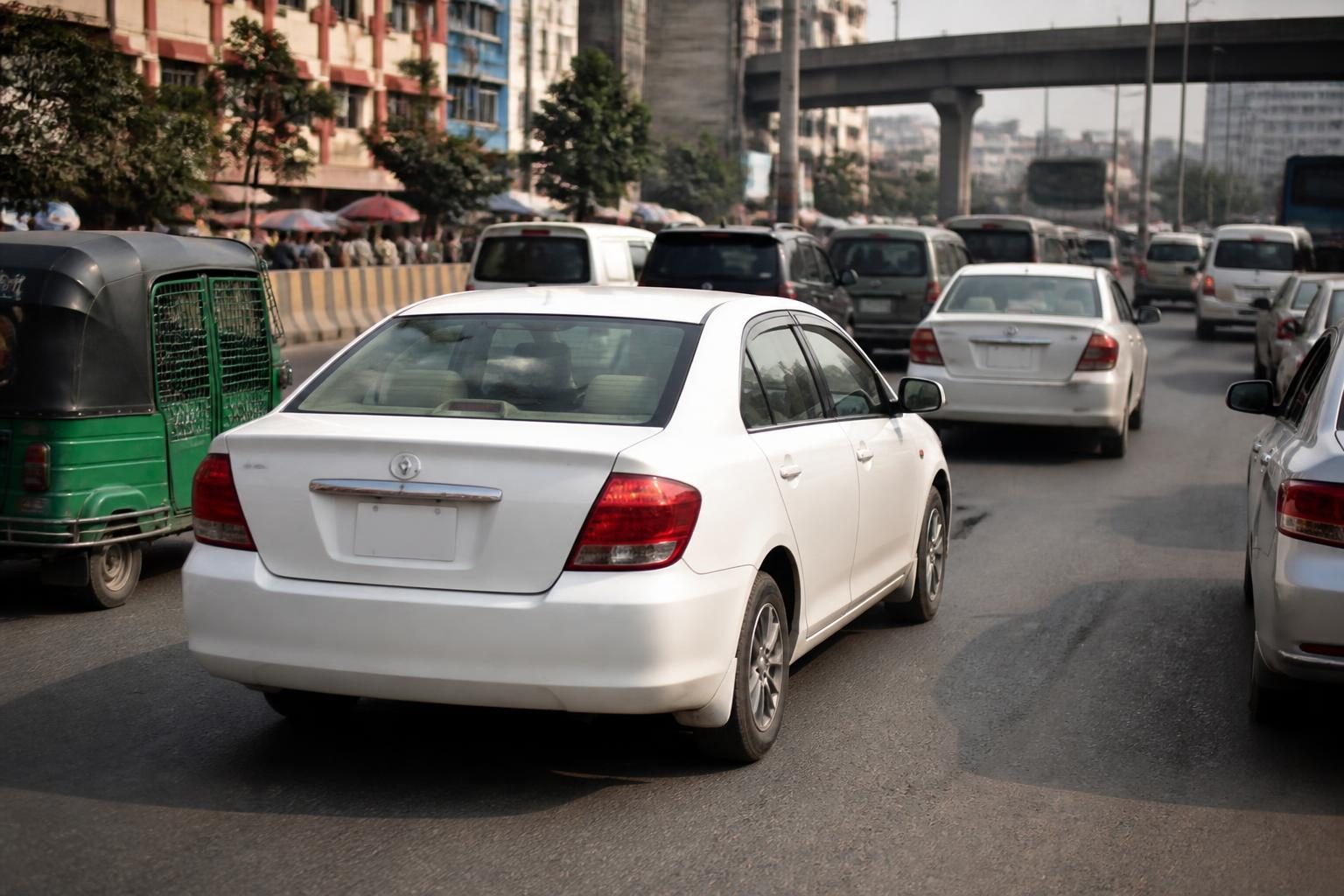 Cars and a green auto-rickshaw queue in heavy traffic beneath an elevated urban roadway.