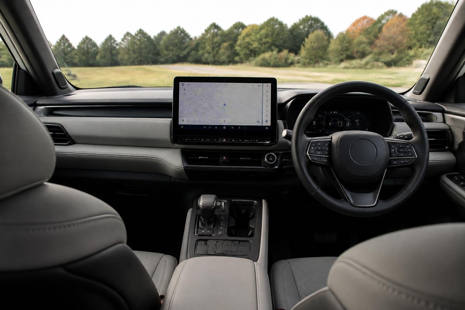 Rear-seat view of a modern right-hand-drive SUV interior with touchscreen and grey leather seats.