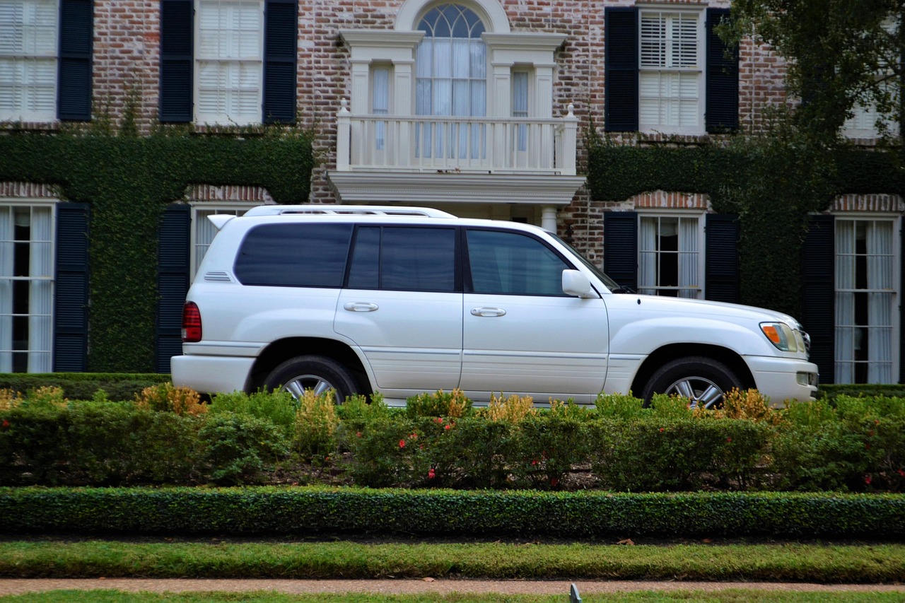 White luxury SUV parked in front of a brick house with hedges and shuttered windows