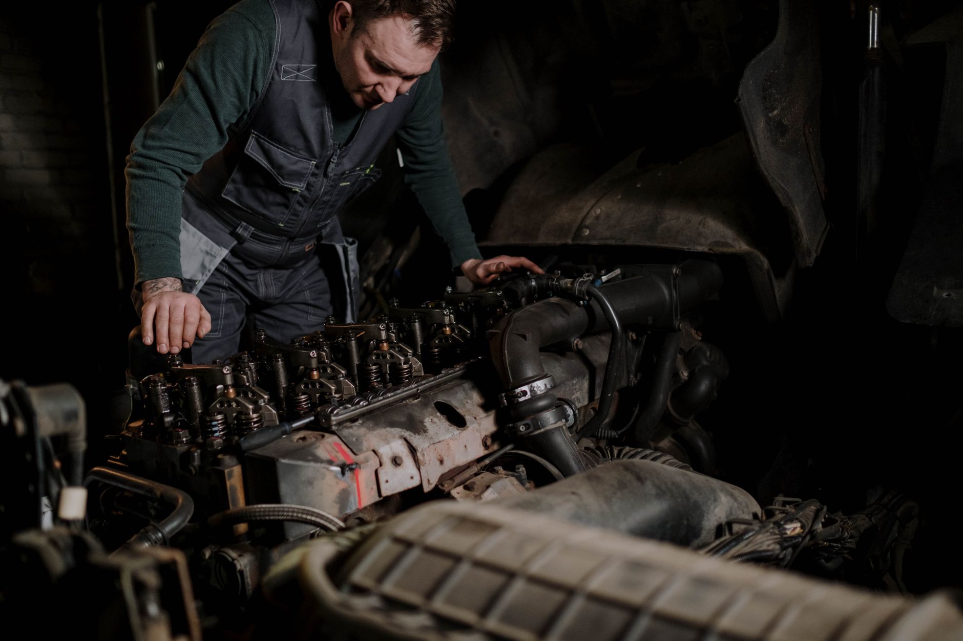 Mechanic leaning over an exposed engine bay in a dim workshop