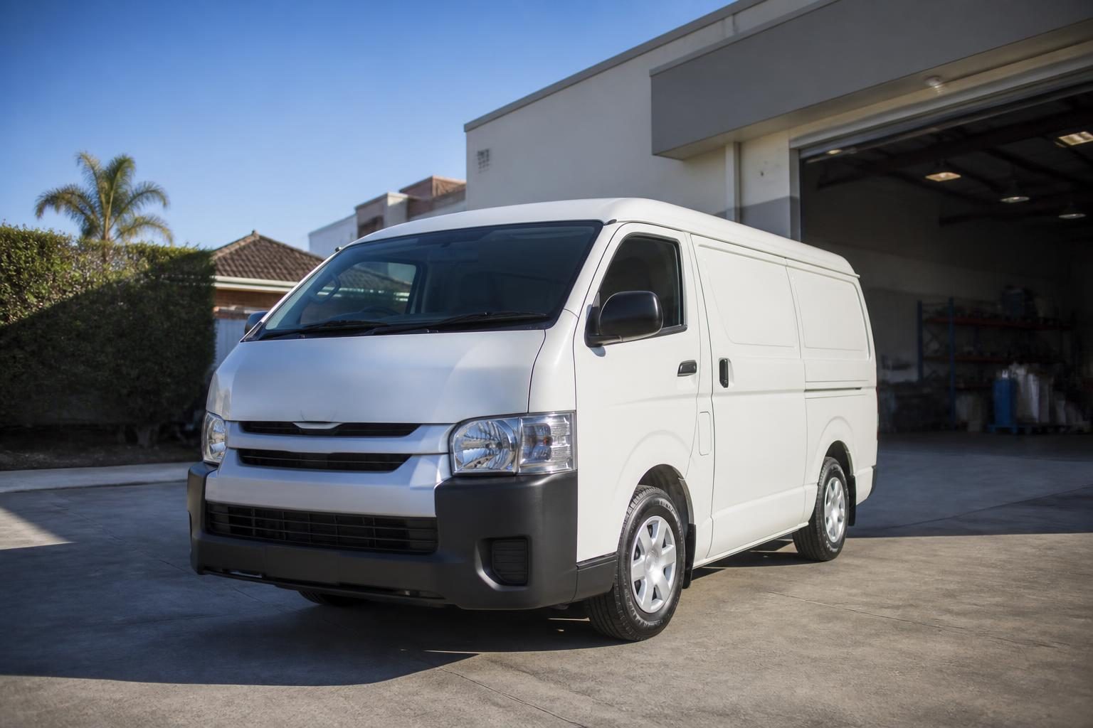 White panel van parked outside a workshop with an open roller door on a sunny day.