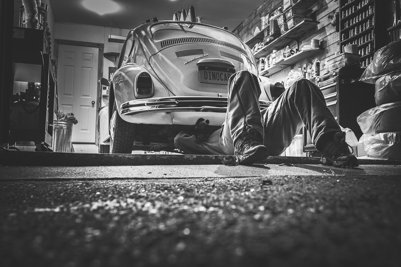 Black-and-white view of a classic Beetle on a lift with a mechanic underneath in a garage