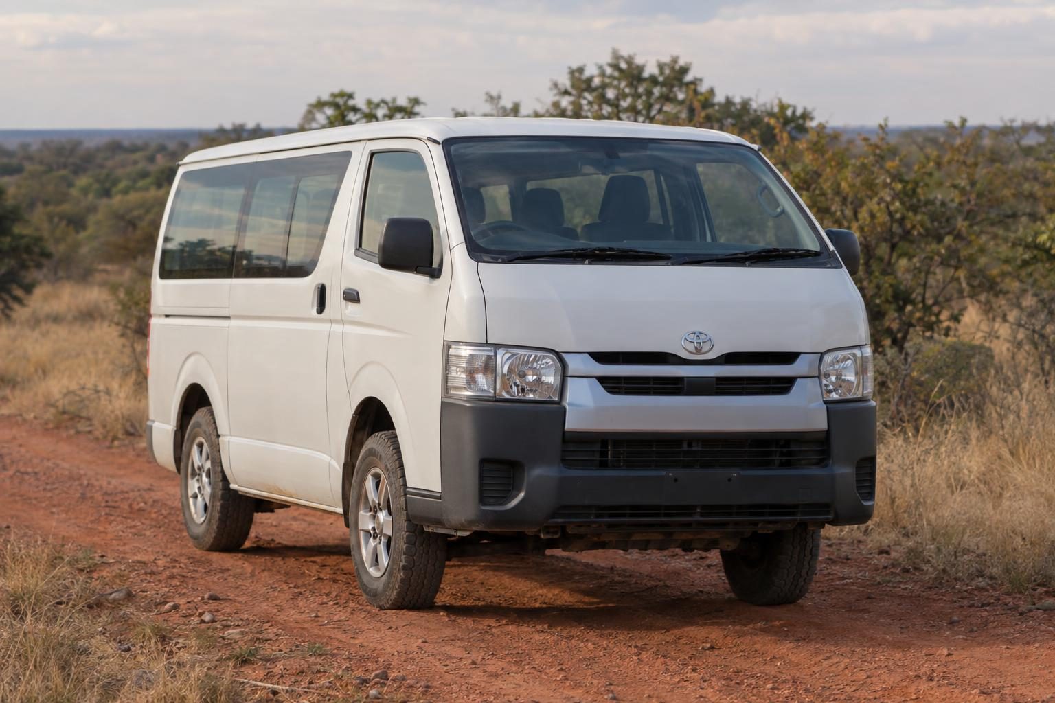 White Toyota Hiace H200 van on a red dirt track through dry scrubland.