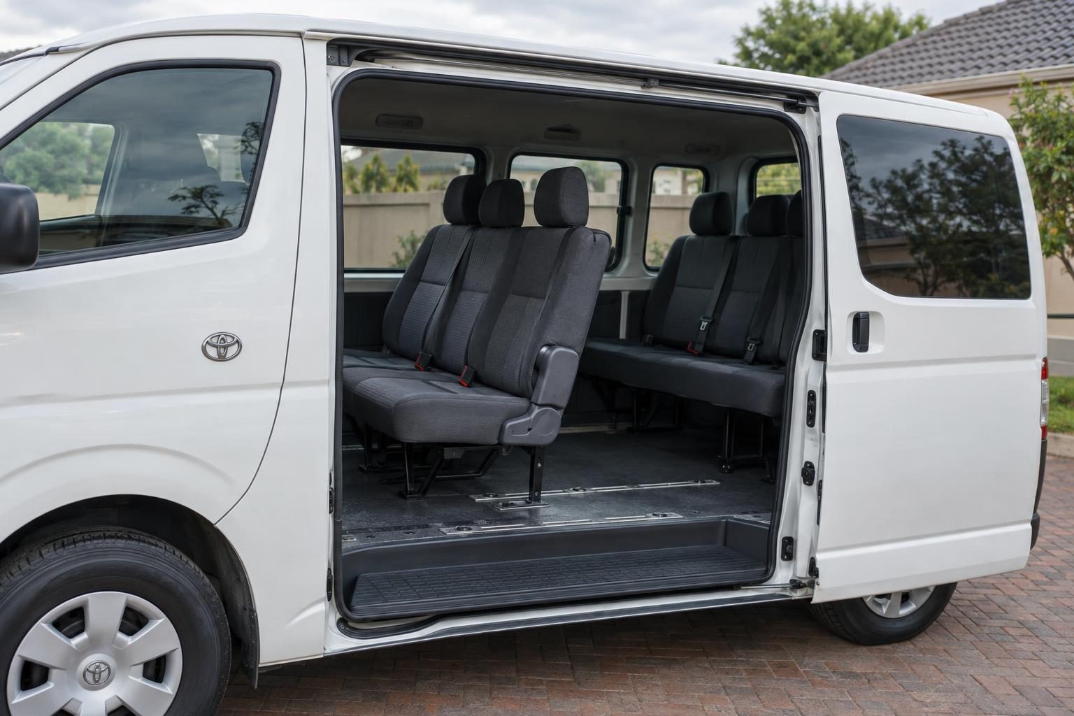 Open sliding door of a white Toyota Hiace H200 passenger van showing seat rows and floor rails.